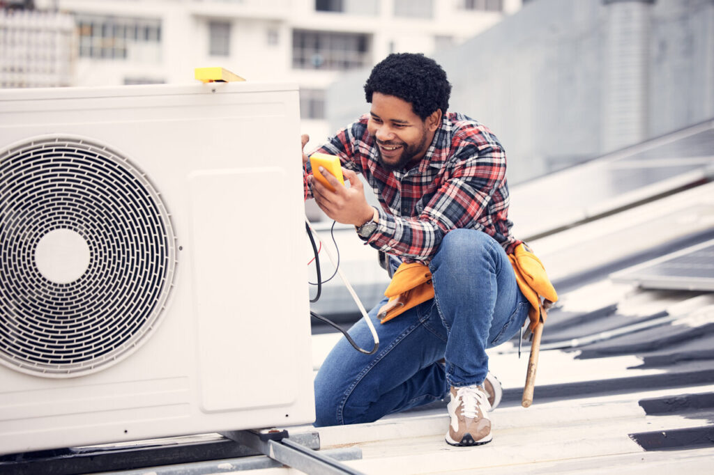 A man repairs an air conditioner, focused on his work with tools in hand.